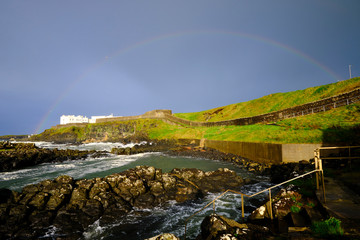 Full rainbow over the rocky coast of Norhern Ireland with rampards  and walkway in background