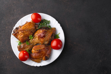 Roasted chicken legs with parsley leaves on a white plate and cherry tomatoes. View from above.