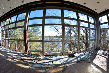 Widok na las i zalew przez wybite i zniszczone okna w opuszczonym budynku przez obiektyw fisheye.