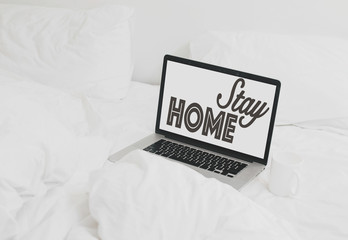 Stay home text on laptop screen and coffee cup on white soft bed.  Isolation at home to prevent virus epidemic. Shopping or working online from home. Freelance and freelancer. Staying home