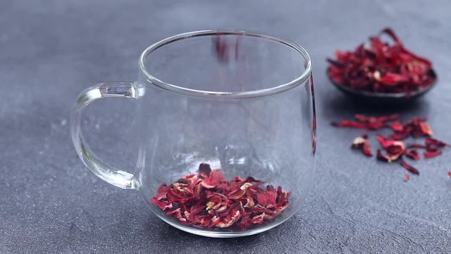Hibiscus tea pouring into a glass cup. Grey background. Close up.