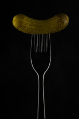 Gherkin on a fork on a dark background
