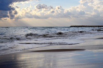 Sunset on the seashore with reflection of cloudy sky on a wet sand on the beach