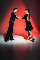 elegant young couple of ballroom dancers in black outfits dancing in red light