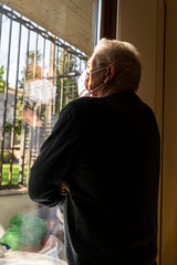mature man with mask looking out the window forced to quarantine