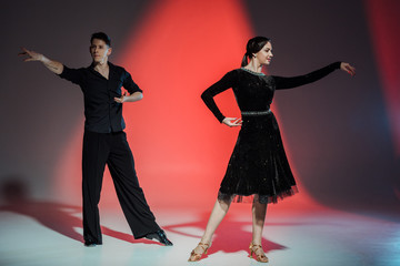 elegant young couple of ballroom dancers dancing in red light