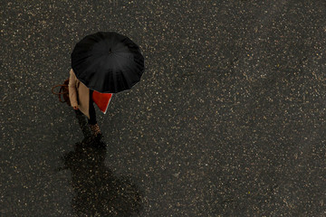 Unknown woman walking with black umbrella on the wet road with copy space.Above view.