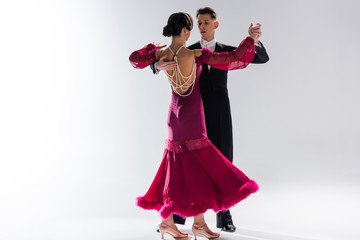 elegant young couple of ballroom dancers in red dress in suit dancing on white