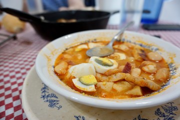 Close up view of a half eaten plate of fabada with eggs over a red and white tablecloth