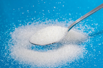 Sugar in a teaspoon. Sprinkle grains of sugar on the blue surface.