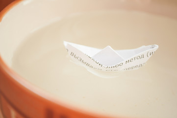 A paper boat floats in a plate with water. Closed water border concept. Short boat trips. Vacation...