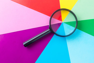 Magnifying glass on multi-colored sheets of paper. Search for diversity color combinations. The...