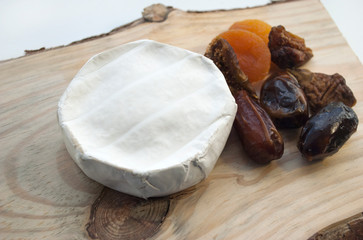 Camembert cheese and various dried fruits: figs, dried apricots, dates. On a wooden background.
