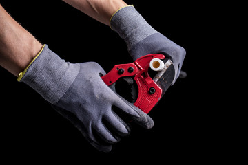 Hands of a plumber in gloves cutting a plastic pipe with a special tool.