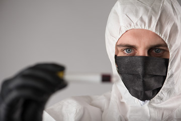 a virologist in a black mask and medical gloves wearing a white protective suit, conducts blood...