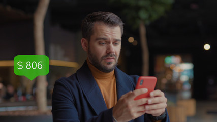 Happy Young Man in Shopping Mall With Christmas Gifts in Hand Uses Smartphone Dance. App Icon With Online Transaction. Financial Transactions in the Smartphone. Receive a Message About Increase Money.