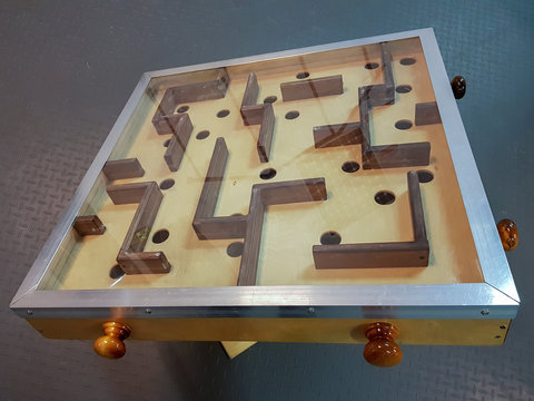 Wooden labyrinth with round holes under the glass with a metal frame on a turning table. 