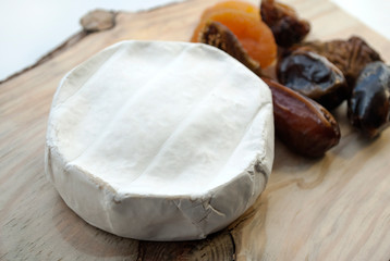Camembert cheese and various dried fruits: figs, dried apricots, dates. On a wooden background.