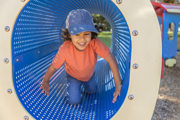 A happy little boy with a smile crawls through a blue tunnel with small holes at the playground....