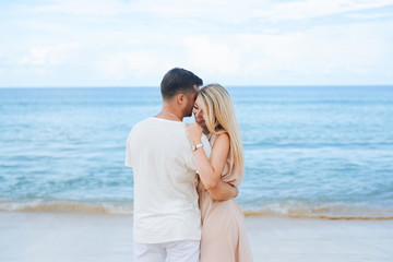 Young attractive man and woman in love walk and hug against the background of white sand and azure sea. Travel, honeymoon