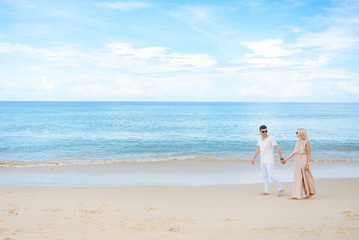 Fototapeta na wymiar Young attractive man and woman in love walk and hug against the background of white sand and azure sea. Travel, honeymoon