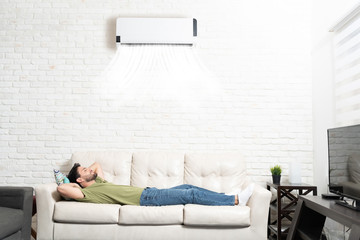 Latin Man Sleeping On Sofa Below Air Conditioner At Home