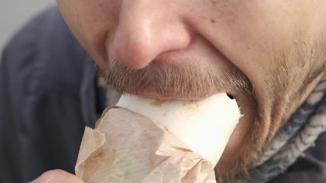 Slow motion close up bearded man eating Doner kebab or falafel shawarma or tortilla roll sandwich outside. Vegan fast food.