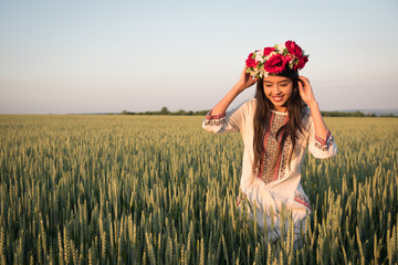 Pretty young woman wear traditional Ukrainian clothes and flower wreath walk in wheat field,...