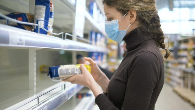 A woman in a medical mask takes the last bag of cereals in the store, empty supermarket shelves.