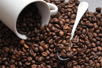 coffee beans are poured from a white Cup. next to the beans is a spoon