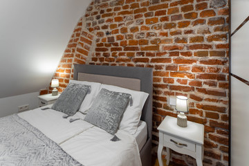 Modern contemporary interior of bedroom. Brick wall. Cozy bed with bedsides.