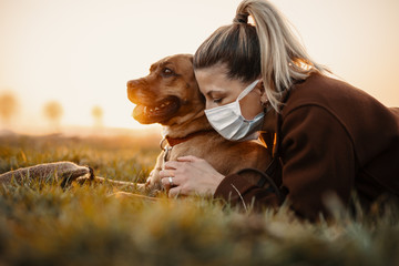 Woman wearing a protective mask is walking alone with a dog outdoors because of the corona virus...