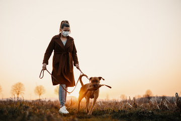 Woman wearing a protective mask is walking alone with a dog outdoors because of the corona virus...