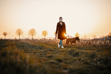 Woman wearing a protective mask is walking alone with a dog outdoors because of the corona virus...