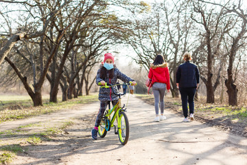 Fototapeta premium Little girl wearing medical mask prevent flu, pollutions and covid-19 riding bicycle outdoor.