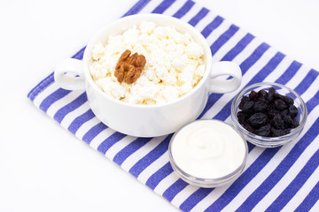 Breakfast concept. cottage cheese with walnuts, raisins and sour cream on a light background and a towel. white