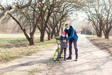 Fototapeta premium Little girl wearing medical mask prevent flu, pollutions and covid-19 riding bicycle outdoor.