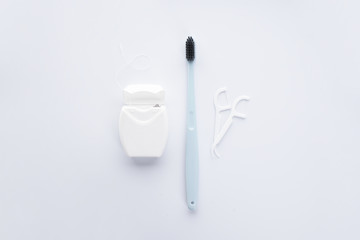 Flat lay composition of blue toothbrush, dental floss and toothpicks on a white background.