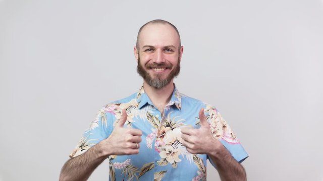 Happy bearded man wearing hawaiian shirt showing thumbs up over white background. Good job, very well.