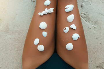 Tanned legs on the sand of the sea, seashells lined on the skin, summer vacation on a tropical...