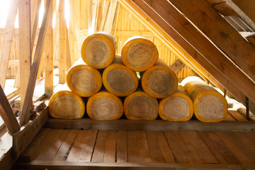 insulation rolls in yellow packaging in the attic of a wooden house.
