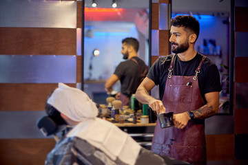 Fototapeta premium Master cuts hair and beard of men in the barbershop, hairdresser makes hairstyle for a young man