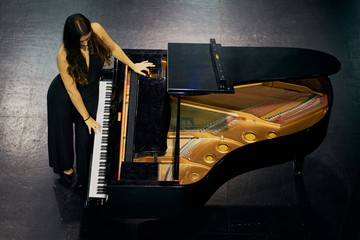 A woman standing playing a grand piano on a stage. View from above
