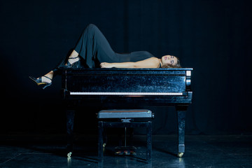 A woman lying on top of a grand piano on a stage