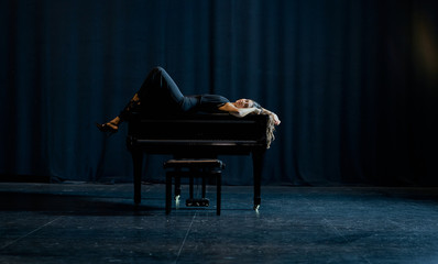 A woman lying on top of a grand piano on a stage