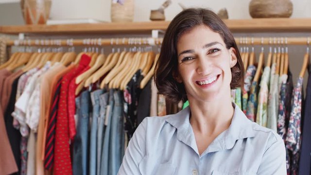 Portrait of female owner of fashion store standing in front of clothing on rails - shot in slow motion
