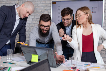 Team of young business people and designers, gathered in front of a laptop computer, working on new projects and discussing new business ideas. Startup concept.
