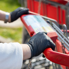 Hände, Handschuhe am Griff von Einkaufswagen, Hygiene beim Einkaufen 