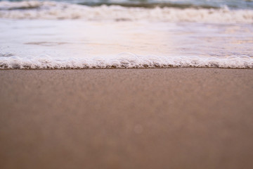 Waves with foam close up on a tropical sandy beach on a sunset. Copy space