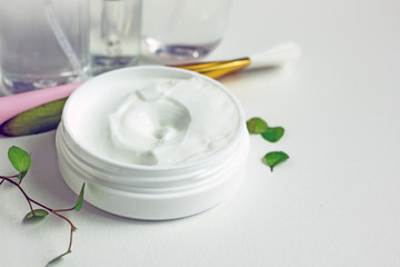 Cosmetic cream jar on a light background. Organic cream face in a white jar with an open lid, a number of face and body care accessories, green leaves of the plant. The concept of skin cream 